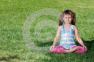 Little child meditate in asana on green grass
