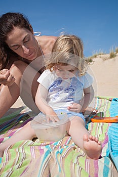 Little child and mother at beach eating from tupperware