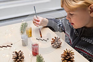 Little child painting pine cones and wooden Christmas tree decorations