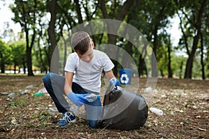 A little child picking up the garbage and putting it in a black garbage bag on a natural background. Ecology protection