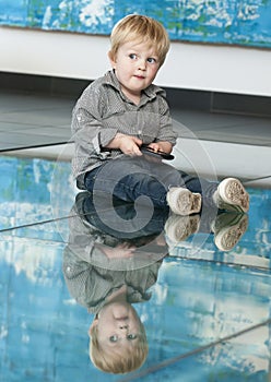 Little child playing with cellphone and his reflexion on the floor