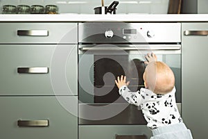 Little child playing with electric stove in the kitchen. Baby safety in kitchen