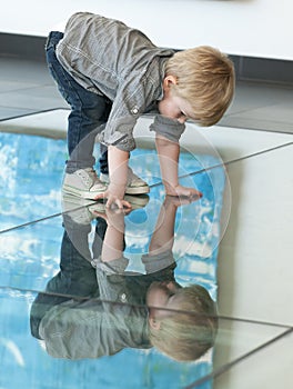 Little child playing with his reflexion on the floor