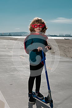 Little child is playing superhero. Boy super hero concept. Child on scooter in park. Kids learn to skate roller board.