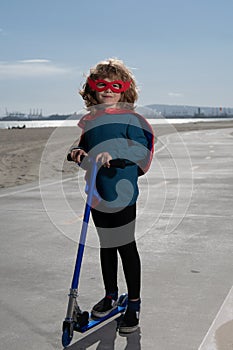 Little child is playing superhero. Boy super hero concept. Child on scooter in park. Kids learn to skate roller board.