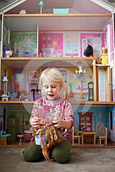 Little Child Playing Toys in Front of a Large Dollhouse in her Bedroom