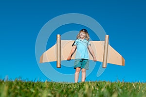 Little child plays astronaut or pilot. Child on the background of blue sky. Kids with paper wings jetpack dreams