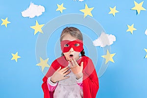 Little child plays superhero. Kid on the background of bright blue wall with white clouds and stars . Girl power concept