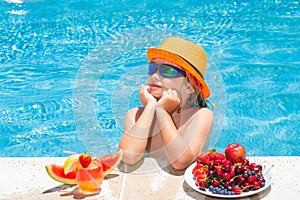 Little child by the pool eating fruit and drinking lemonade cocktail. Summer kids vacation concept.