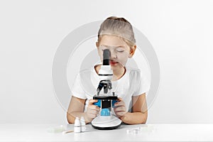 Little child prodigy girl looks through a microscope  studying in the laboratory. Interesting experiments for children
