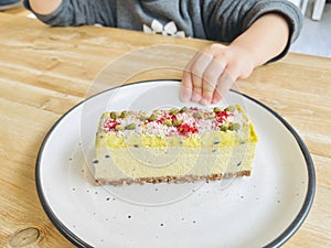 A little child reaches for the yellow mango rectangular cake.