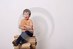 Little child reading book and in bewilderment covers mouth. Kid with glasses sitting on books.