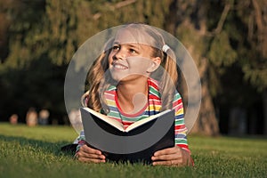 Little child reading book outdoors. Schoolgirl reading stories while relaxing green lawn. Cute pupil enjoy reading