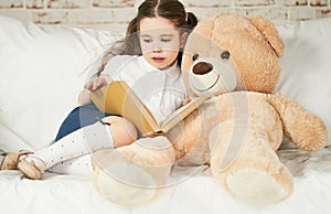 Little child reading to her plush friend