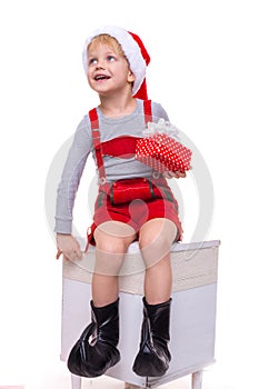 Little child in red costume of dwarf holding gift box with ribbon and looking up. Christmas