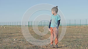 Little child refugee with dirt on his clothes. area of the refugee camp encircled by a high fence, poor boy holding plush bunny an