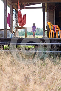 Little child running on a wooden house porch at summer, focus at the steps with dry yellow grass