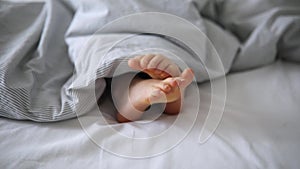 Little child's feet in bed covered with blanket
