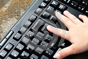 Little child`s finger pressing the enter key on a black pc keyboard. Small kids hand, pressing enter key. Confirmation, accepting