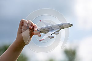 Little child`s hand holds white metal airplane model pretending he is flying Boing plane in clear blue sky with clean white fluff