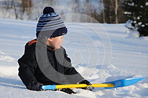 Little child with shovel sitting on snow