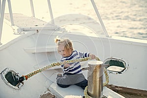 Little child sitting and berthing rope on white boat