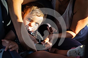 Little child sitting in a car seat while his mother ties his belt