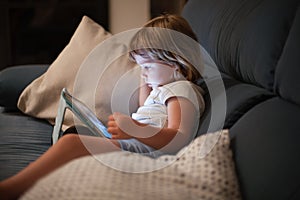 Little child sitting comfortably in sofa watching tablet