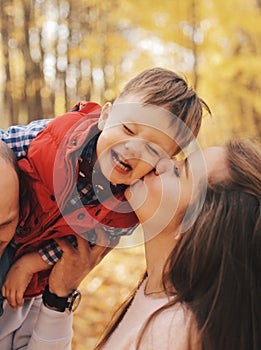 Little child sitting on father`s shoulders. Mother kisses her son