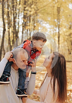 Little child sitting on father`s shoulders. Mother kisses her son