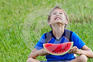 Little child sitting on green grass in park and eating watermelon
