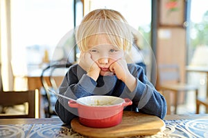 Little child sitting the table in cafe or restaurant and doesn`t want to eat. Healthy food. Kids diet. Poor appetite