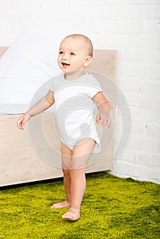 Little child smiling and walking through light room with bed and green carpet