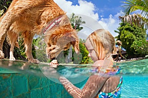 Little child swim with dog in blue swimming pool.