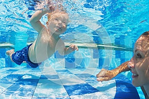 Little child swimming underwater in pool with mother