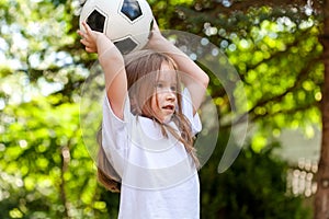 Little child throwing a ball from over her head. Girl playing with a football in a park, portrait. Young sporty kid