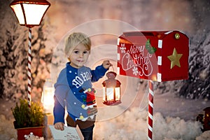Little child, toddler boy, sending letter to santa in christmas mailbox, christmas decoration around him, outdoor snow shot
