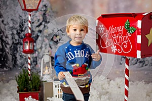 Little child, toddler boy, sending letter to santa in christmas mailbox, christmas decoration around him, outdoor snow shot