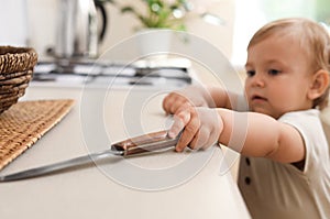 Little child touching sharp knife indoors. Dangers in kitchen