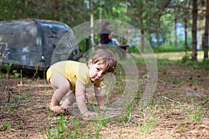 Little child trying to stand up while walking barefoot in evergreen forest with her mother