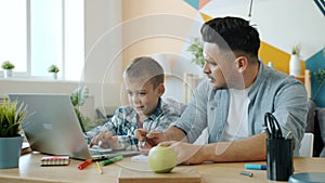 Little child using laptop while father talking to him teaching at home at desk