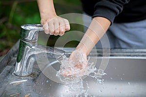 Little child washing hands with clean running water in the park. Flowing water from tap. Metal washing basin outdoor. Coronavirus