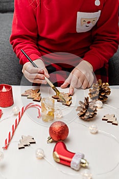 Little child wearing christmas holiday pajamas, doing crafts, painting Christmas tree decorations