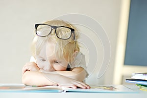 Little child wearing glasses is having fun with a book. Cute boy is watching pictures and learning letters. Preparation for school