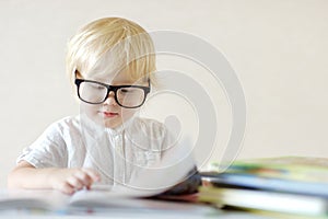 Little child wearing glasses is having fun with a book. Cute boy is watching pictures and learning letters. Preparation for school