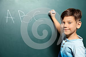 Little child writing letters on green blackboard