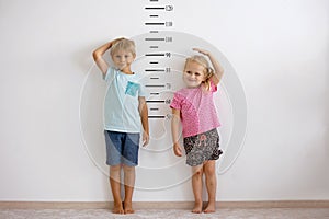 Little children, blond boy and girl, measuring height against wall in room