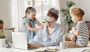 Little children distracting dedicated young woman working on laptop at home