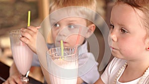 Little children drink fruit milkshakes in a cafe.