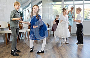 Little children in elegant dresses practicing rock-n-roll dance in school hall